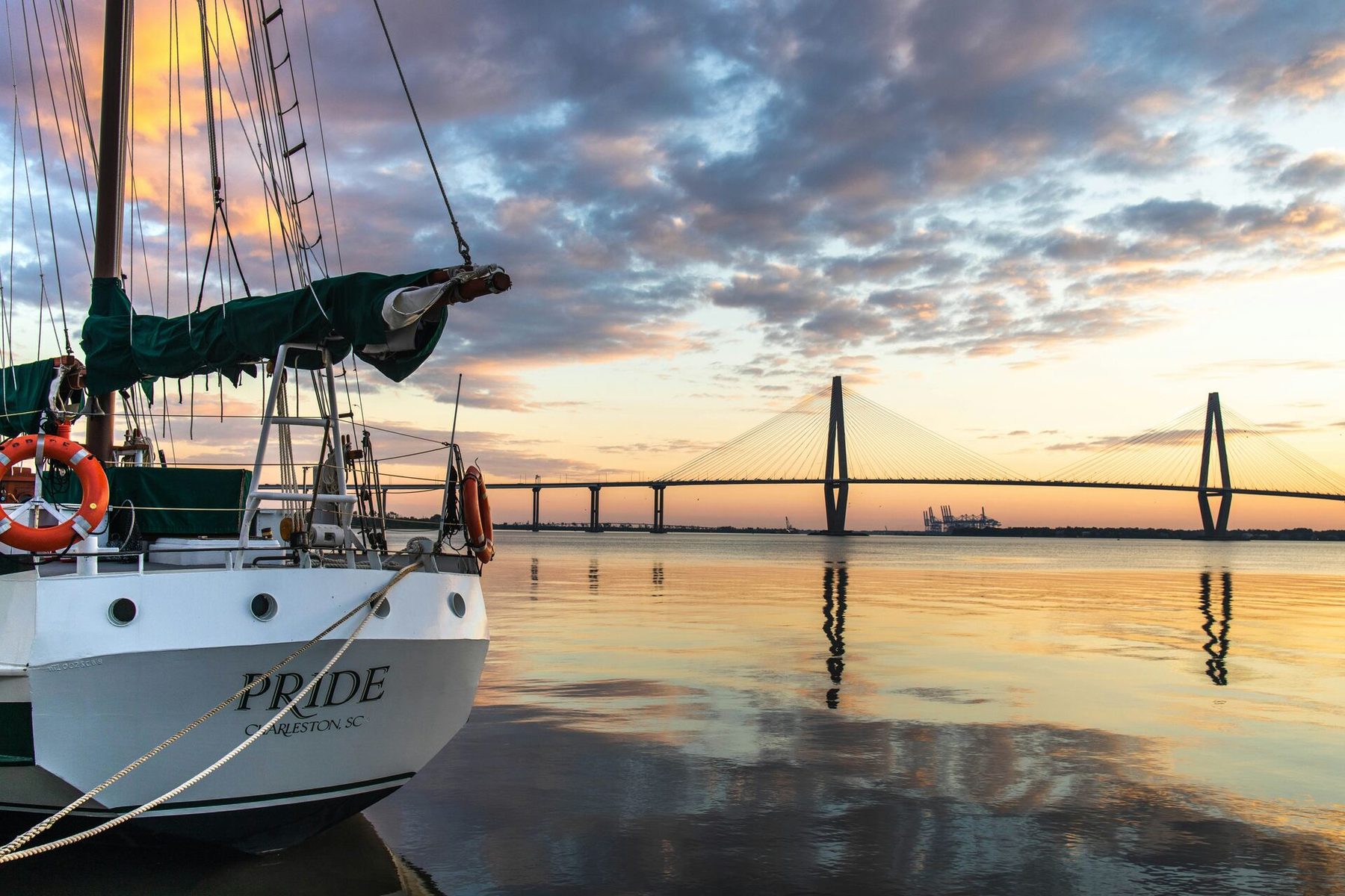 A schooner at dock in Charleston Harbor with the Ravenel Bridge at sunset